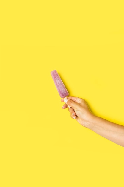 Woman hand holding water popsicle on a yellow background with copy space