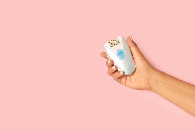 Woman hand holding a wet and dry electric shaver on a pink background with copy space