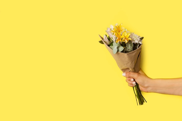 Woman hand holding a yellow and white flowers bouquet on a yellow background with copy space