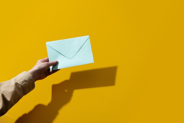 Woman hand holds blue envelope on yellow surface