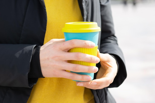 Photo woman hand holds eco coffee cup on a city street background,take away coffee. breakfast on the go.