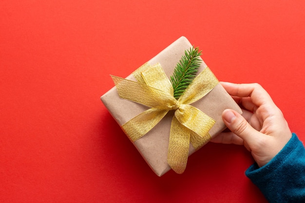 Woman hand holds a present decorated in minimalistic style on red