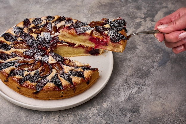 Woman hand holds shoulder blade with piece of plum tart or pie close up selective focus