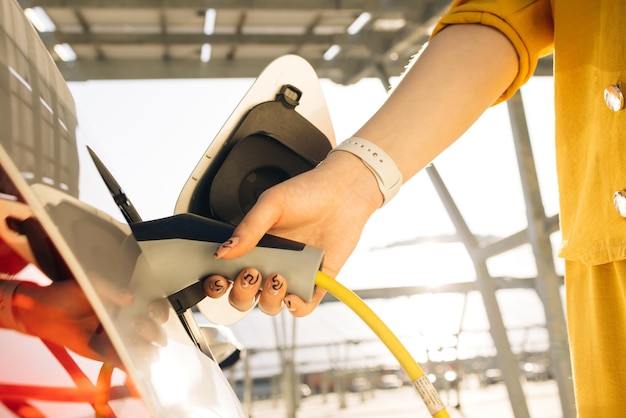 Woman hand inserts power cable supply to charge electric or ev car female plugging an electric car