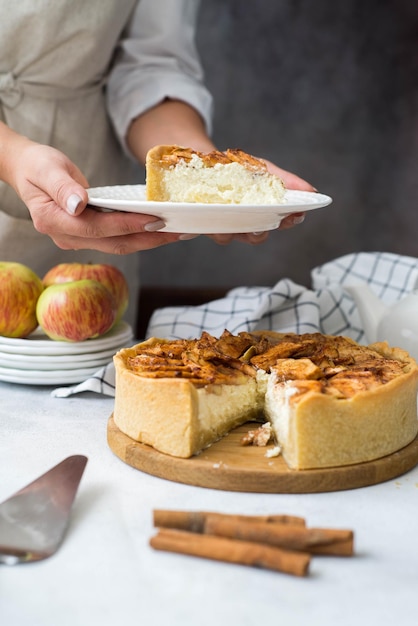 Woman hand is holding a piece of apple pie with cinnamon on white plate