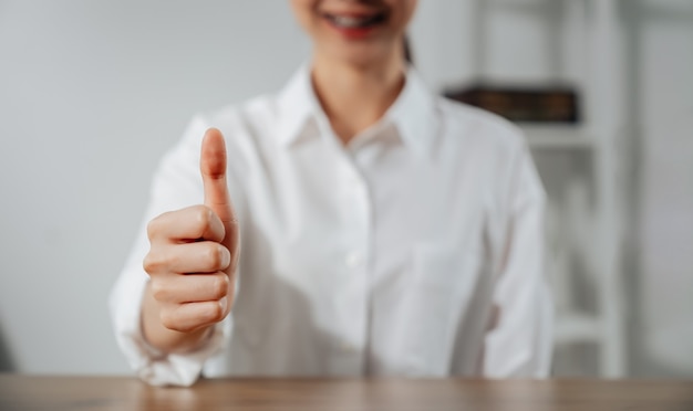 Woman hand making thumb up sign and smiling on the table.