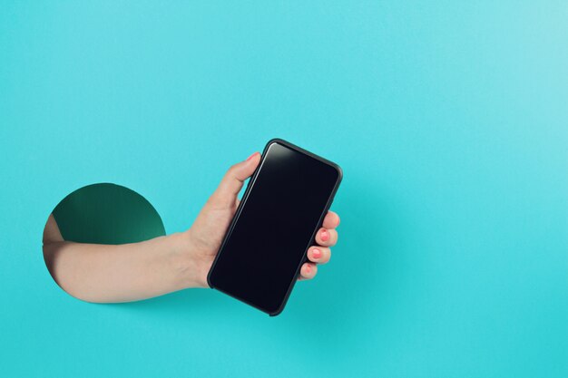 Woman hand in the paper hole holding smartphone