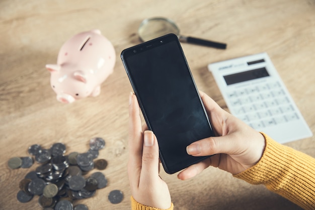 Woman hand phone with coins and calculator on table