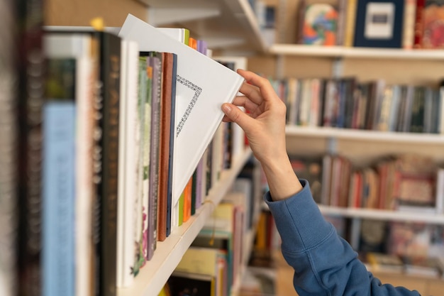 Woman hand picking book from bookshelf in library in university college high school or bookshop