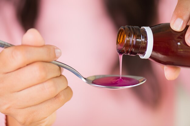 Photo woman hand pouring antipyretic syrup from bottle to spoon. healthcare concept.