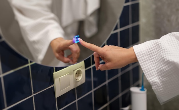 Woman hand pressing button for turning on light and heating mirror in bathroom closeup