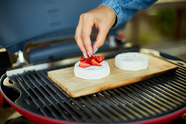 Woman hand put strawberry on grill camembert cheese outdoor