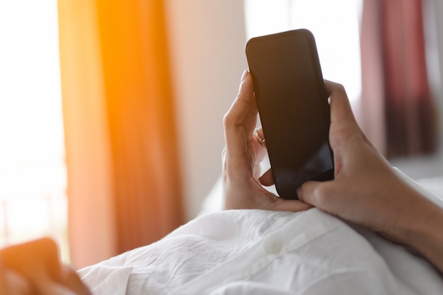 Woman hand using smartphone with blank screen while lying in bed at morning.