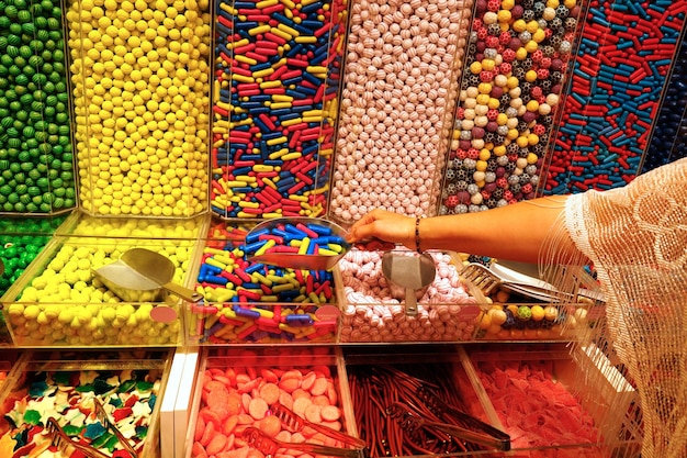 Woman hand with scoop taking colorful delicious candies on counter of shop grocery market cafe