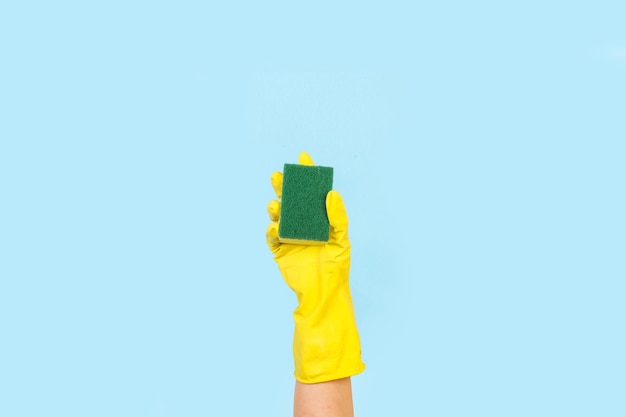 Woman hand with yellow rubber glove holding a cleaning sponge on a light blue background