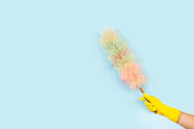 Woman hand with yellow rubber glove holding a multicolor duster on a light blue background