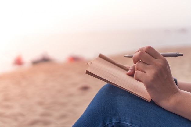 Woman hand writing down in small white memo notebook.