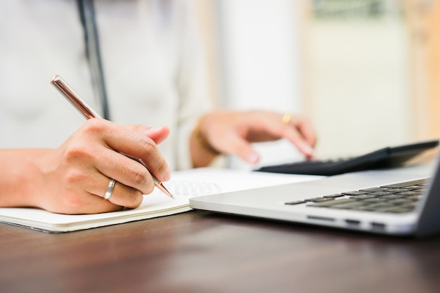 woman hand writing on notebook and pressing on calculator at office 