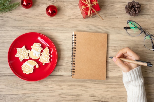 Woman hand writing on notebook with Christmas cookies on table Xmas Happy New Year Goals Resolution To do list Strategy and Plan concept