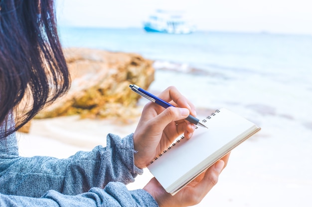 Woman hand writing on a notepad with a pen at the beach