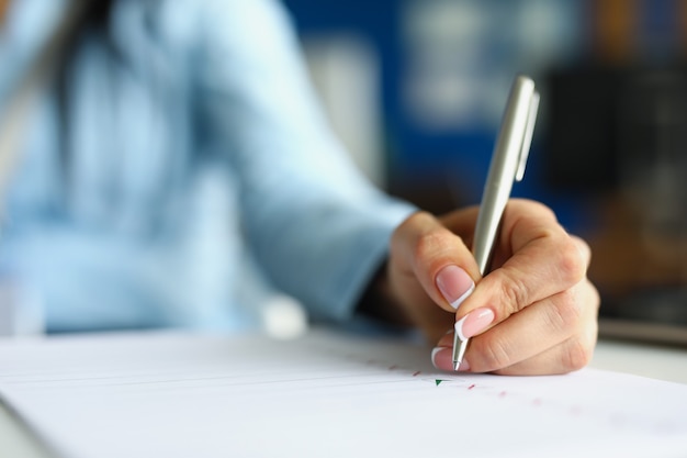 Woman hand writing with silver ballpoint pen in notebook closeup