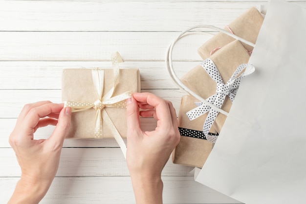 Woman hands are wrapping presents in a gift bag on white surface, top view