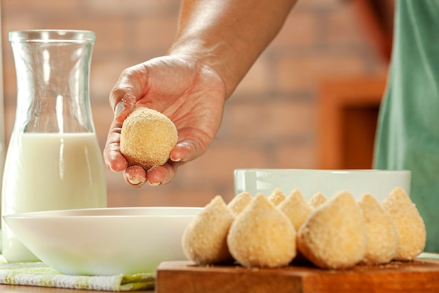 Woman hands breading brazilian croquette coxinha de frango with breadcrumbs on a wooden kitchen table