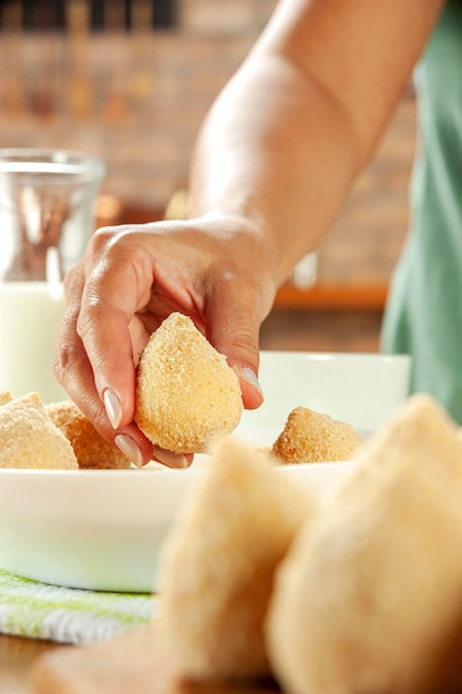 Woman hands breading brazilian croquette coxinha de frango with breadcrumbs on a wooden kitchen table