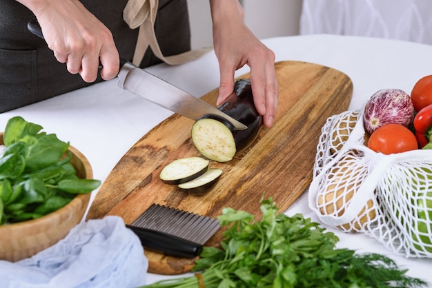 Woman hands cut eggplant with knife on wooden board the process of cooking