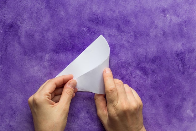 Woman hands folding paper triangle to make smaller triangle on the violet surface