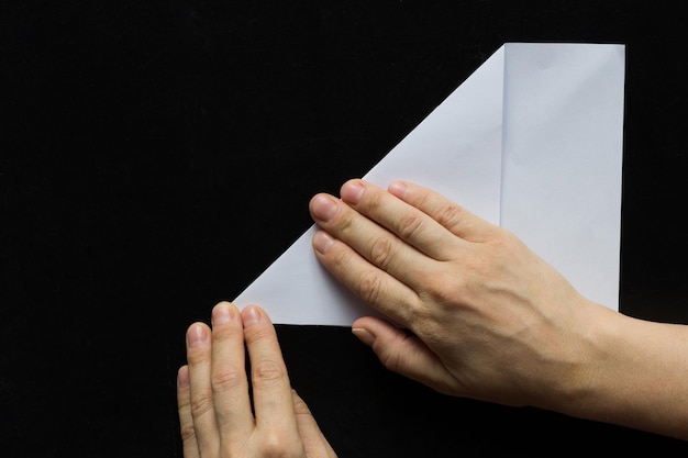 Woman hands folding rectangular sheet of paper to make it square on the black background