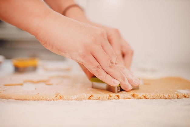 Woman hands form molds cutters ginger dough and makes delicious christmas ginger cookies Cooking and decorating christmas dessert