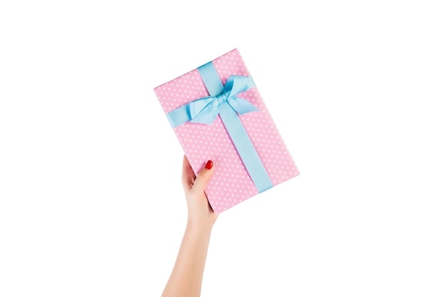 Woman hands give wrapped Christmas or other holiday handmade present in pink paper with blue ribbon. Isolated on white background, top view. thanksgiving Gift box concept.