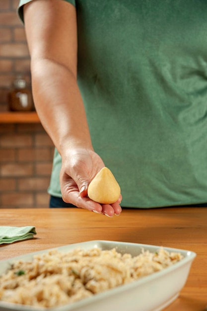 Woman hands holding brazilian croquette coxinha de frango on a wooden kitchen table