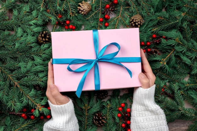 Woman hands holding christmas gift or present box decorated fir tree Preparing for holidays and celebration Female hands holding gift or present box