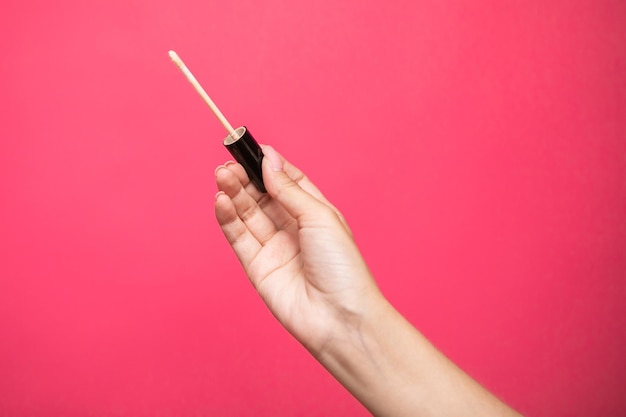 Woman hands holding concealer applicator isolated on pink background