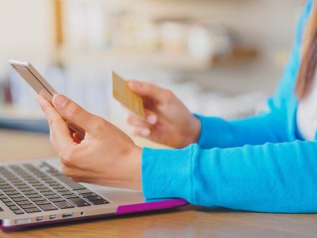 Woman hands holding a credit card and using smartphone and laptop computer.