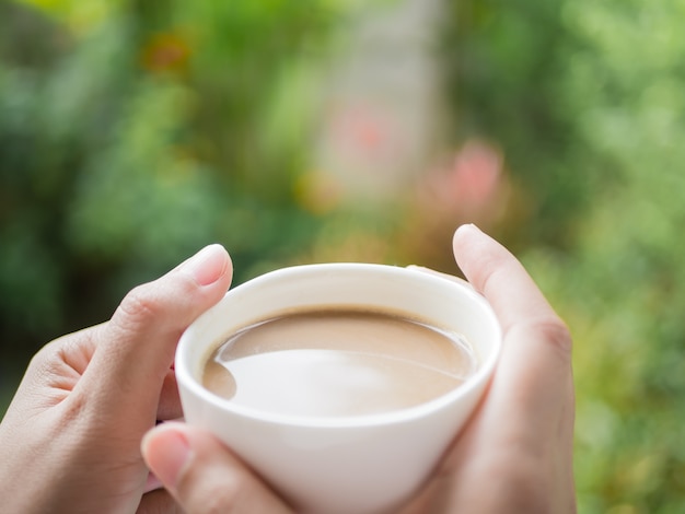 Woman hands holding a cup of coffee at the garden in the morning