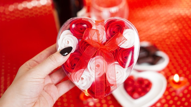 Woman hands holding a gift box in heart shape with beautiful roses over red festive. Concept of giving a gift on Valentines day holidays