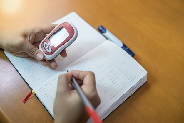 Woman hands holding Glucose meter and use pen to write schedule check blood sugar level 