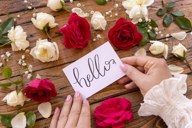 Woman hands holding HELLO card near flowers on a wooden table close up