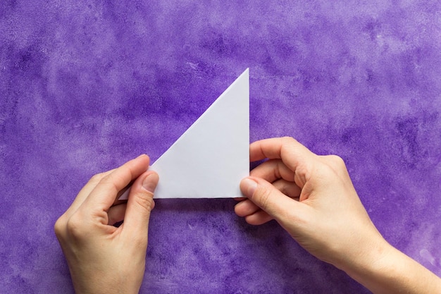 Woman hands holding made folded paper triangle on the violet surface