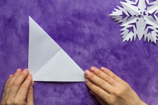 Woman hands holding made folded paper triangle on the violet surface