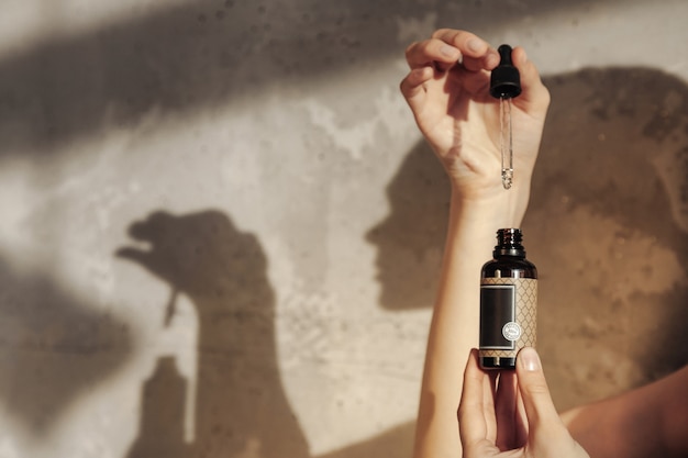 Woman hands holding massage or cosmetics oil bottle. Close-up essential oil in hands. High angle view of massage oil bottle on old background. Concept of healthy lifestyle and self care. Copy space