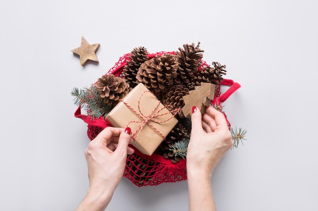 Woman hands holding mesh bag with Christmas zero waste decor sustainable gifts cones and fir tree branches for handmade design