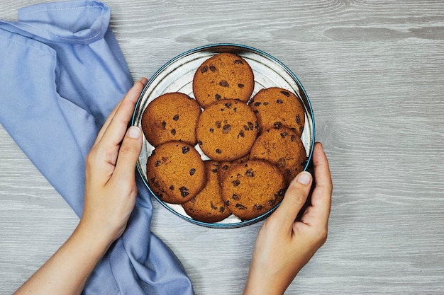 woman hands holding a metal box of pieces of chocolate cookies on wood table