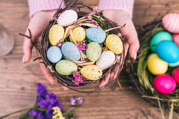 Woman hands holding painted easter egg in a small nest toned picture top view selective focus