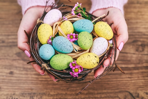 Woman hands holding painted easter egg in a small nest toned picture top view selective focus