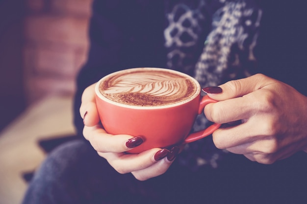 Woman hands holding red cup of coffee latte