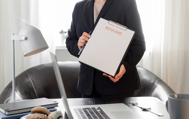 Woman hands holding resume application near her workplace with laptop.